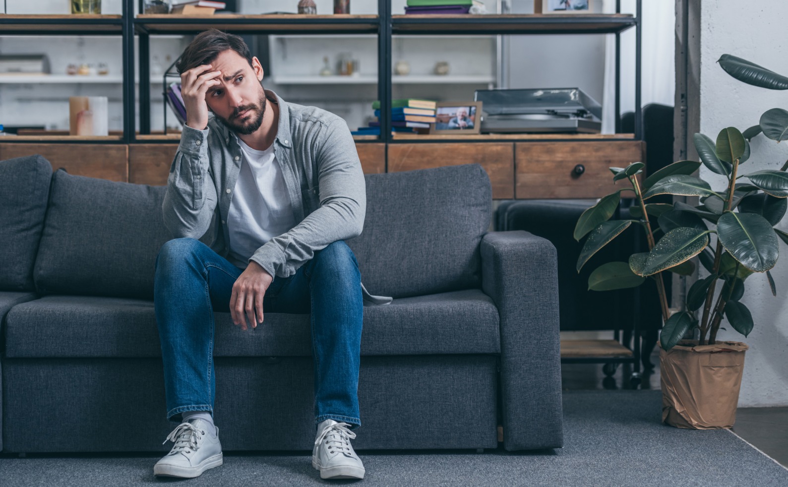 depressed man sitting on couch touching face and grieving at home picture id1145223275