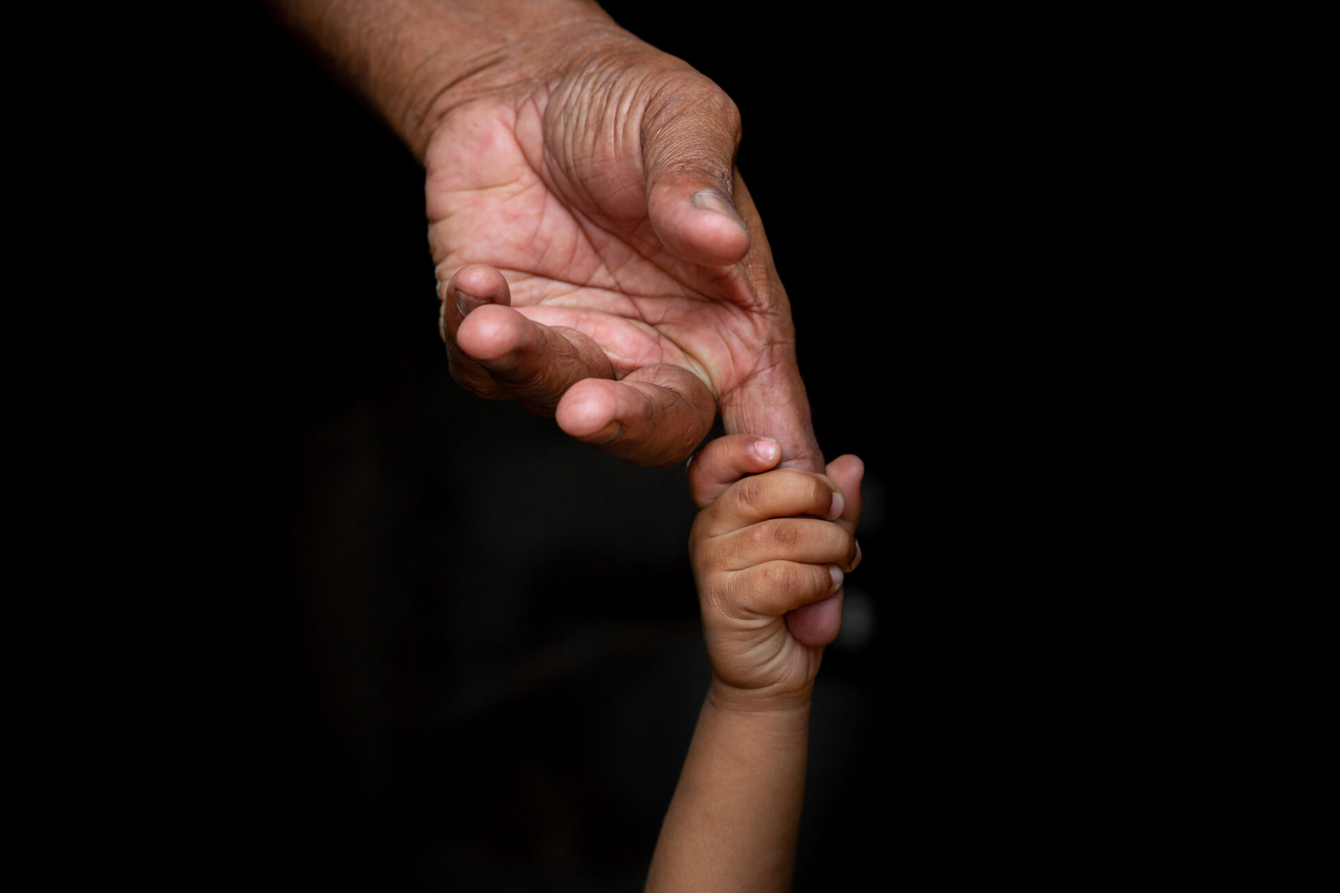 A baby's hands holding tightly A senior man's old age finger. Family, Generation, Support and people concept. Dark background.